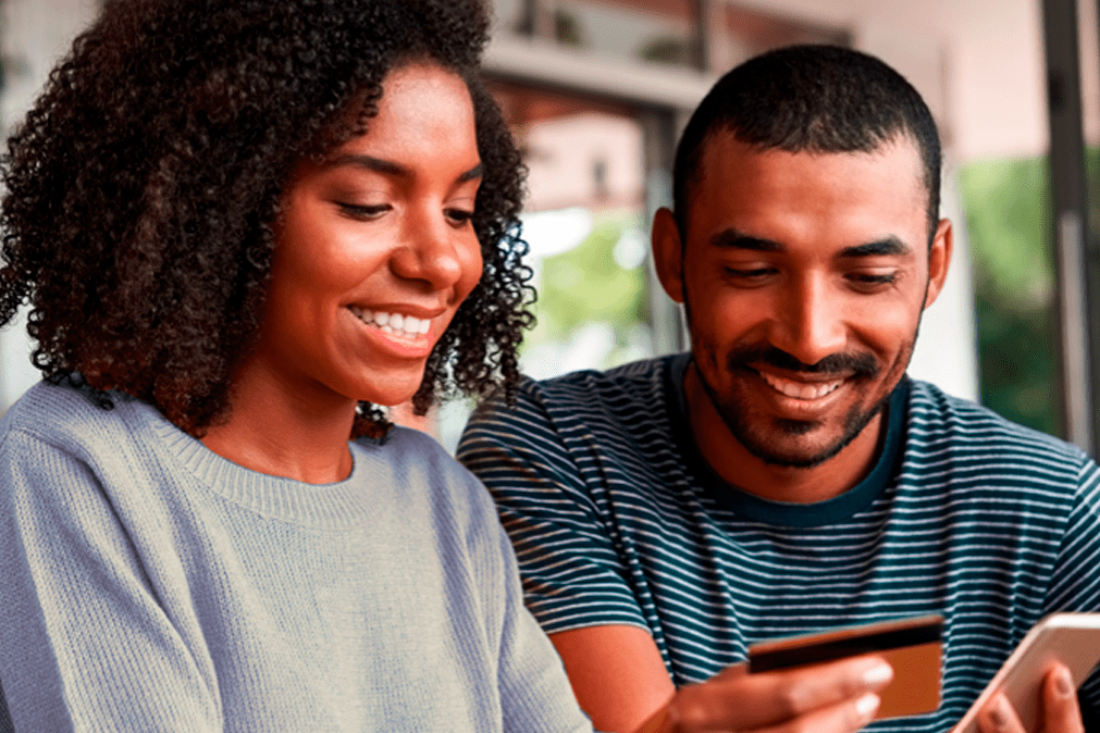 Casal sentado em um sofá sorrindo, pois contrataram o empréstimo pessoal do Agibank.
